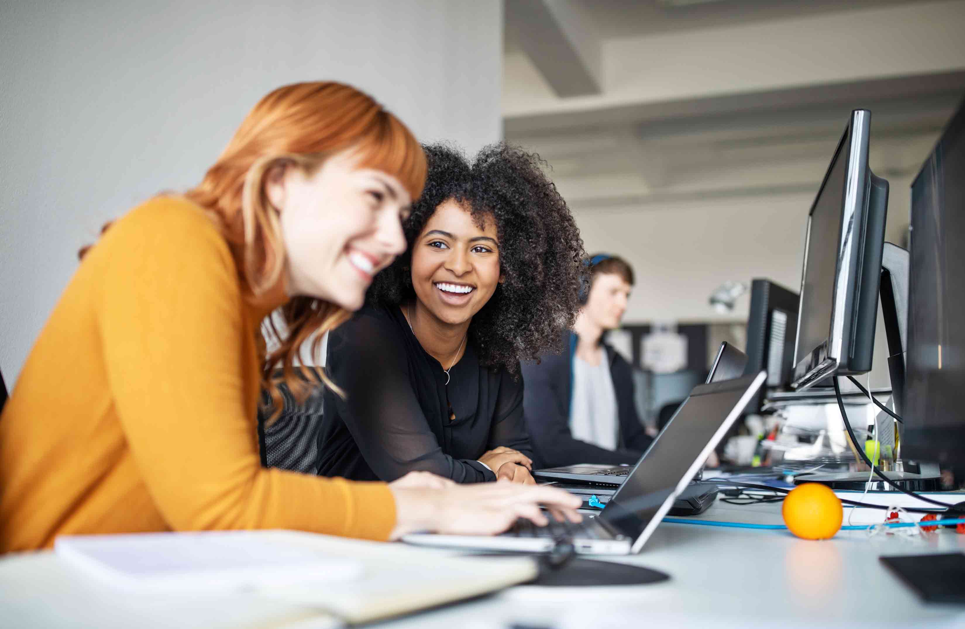 Two smiling young women working on laptop